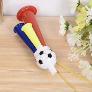 Corneta de aire de tres chorros con base de balón de fútbol, tubos rojo, azul y amarillo, y cordón amarillo sobre madera clara.